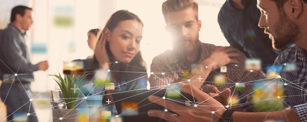 Imagem de três pessoas conversando, uma delas segurando um tablet, explicando algo para os outros dois