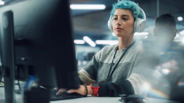 uma mulher sentada em frente ao notebook. Ela aparenta estar trabalhando. A imagem sugere a interação entre o usuário e as ferramentas de IA.