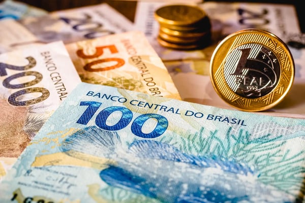 Na imagem, estão algumas notas do Real, moeda brasileira, e moedas de metal de 1 Real. O texto explica o que é Drex, a versão digital do Real.