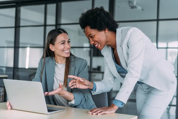 A imagem apresenta duas executivas jovens, uma mulher branca e outra afro-americana, ambas trajando roupas formais. Estão conversando em um escritório. O tema do artigo é captação de recursos para startups.