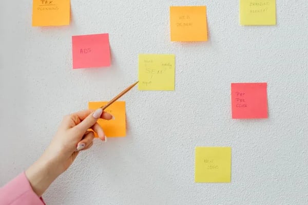 mão apontando com um lápis para post it com planejamento de startups