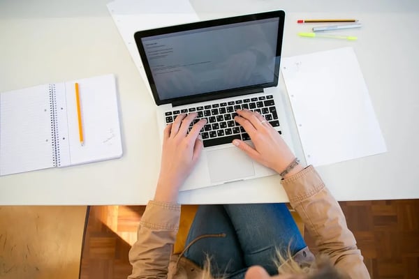 pessoa escrevendo em computador com caderno ao lado