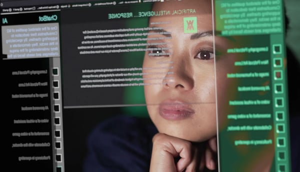 A imagem apresenta uma mulher jovem asiática que olha para a tela de um computador. Por sua vez, de forma tridimensional, é projetado no rosto da mulher o que parece ser a tela inicial de um software de Inteligência Artificial Generativa. O tema do post é futuro do trabalho.