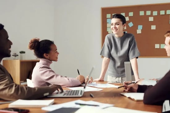 mulher de frente a uma mesa realizando reunião com outras pessoas