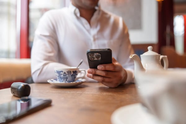 A imagem apresenta uma mão de um homem negro, que manuseia um iPhone. Ele está tomando um café, mas não é possível ver o rosto da pessoa. O tema do artigo é inovação radical.