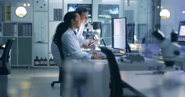 A imagem apresenta duas mulheres jovens e cientistas que estão em um laboratório, analisando imagens em um computador. O tema do artigo é saúde digital.