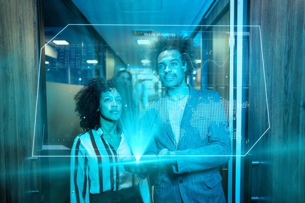 um homem e uma mulher estão em frente a um holograma, que ilustra um painel com mapas e infográficos.