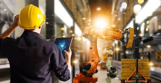 homem de costas com capacete olhando para tablet e máquina de logística
